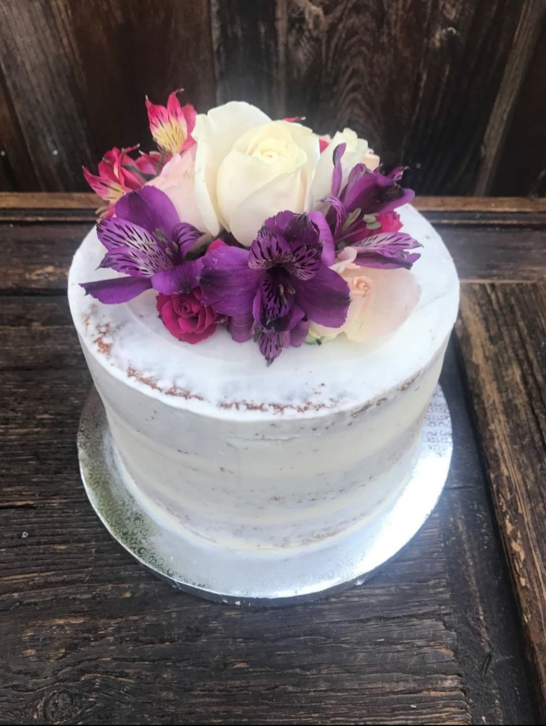 Naked cake decorated with purple, pink, and white flowers on a wooden table.