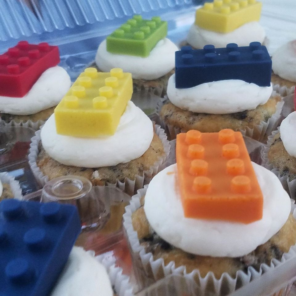 Cupcakes topped with colorful Lego-shaped candies arranged in a clear container.