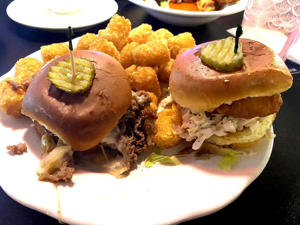 A plate of food with two sliders and tots on a table.