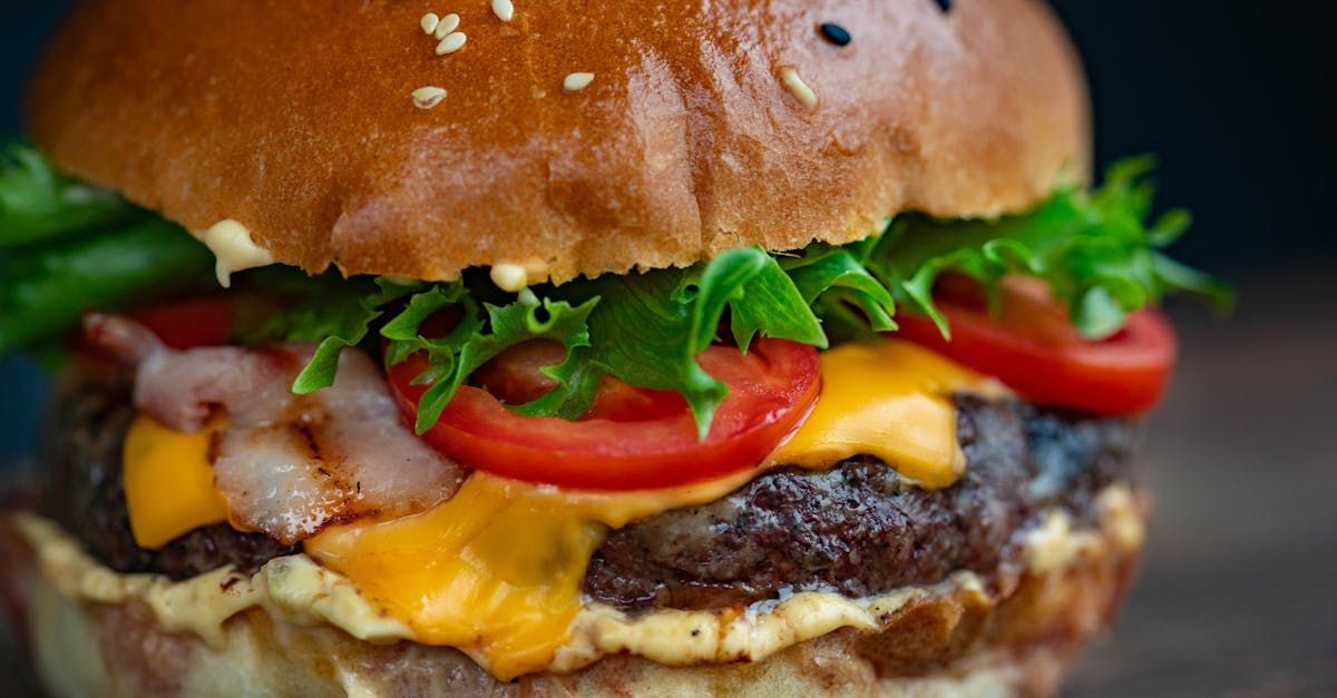 A close up of a hamburger with cheese , lettuce , tomatoes and bacon on a wooden table.