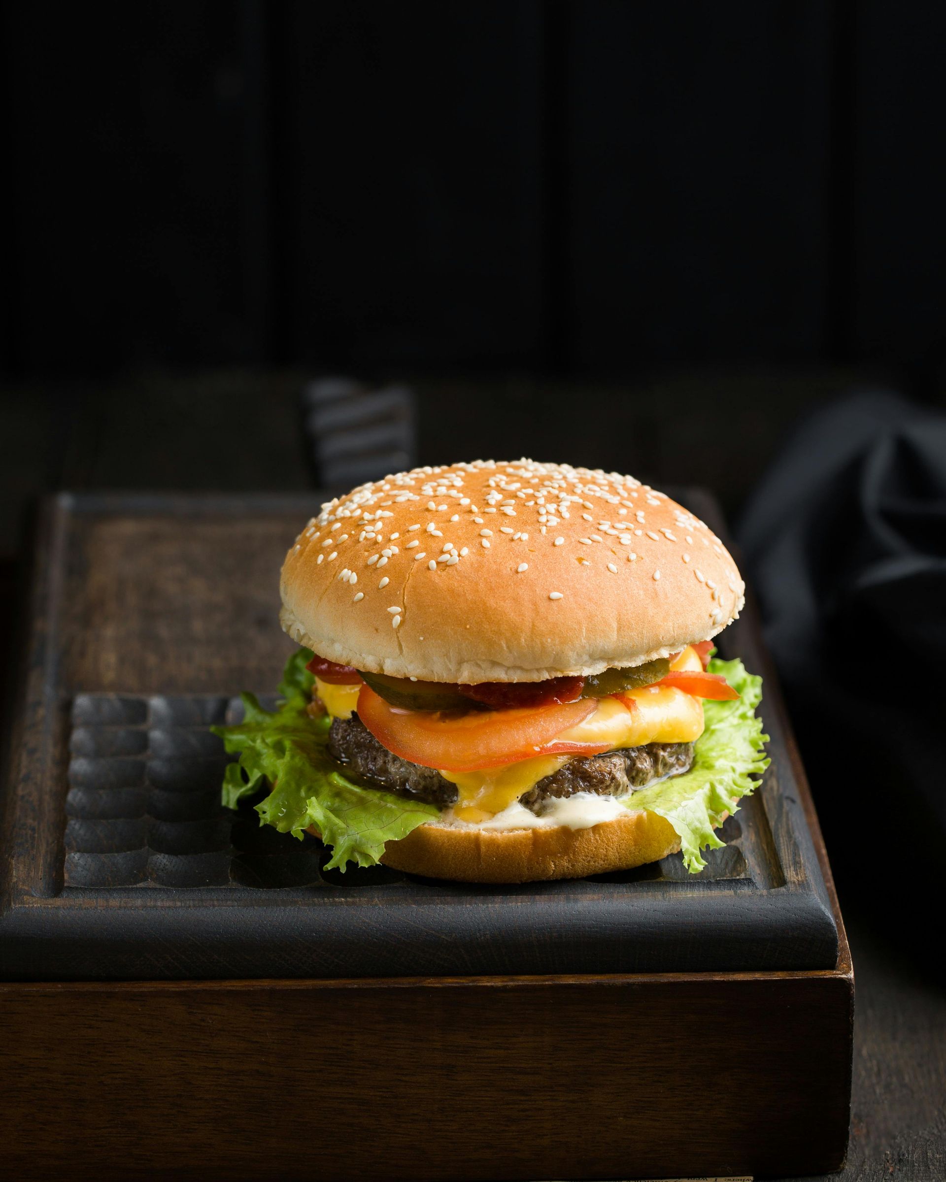 A hamburger is sitting on a wooden tray on a wooden table.