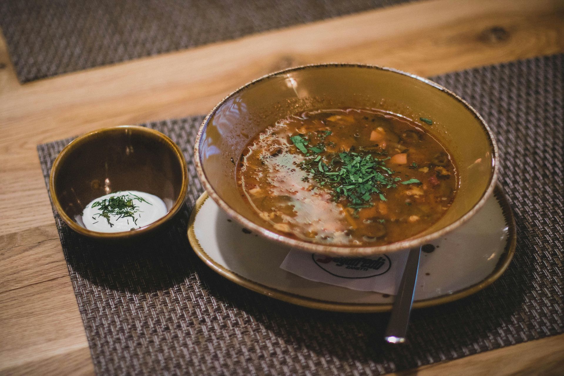 A bowl of soup is sitting on a table next to a bowl of sour cream.