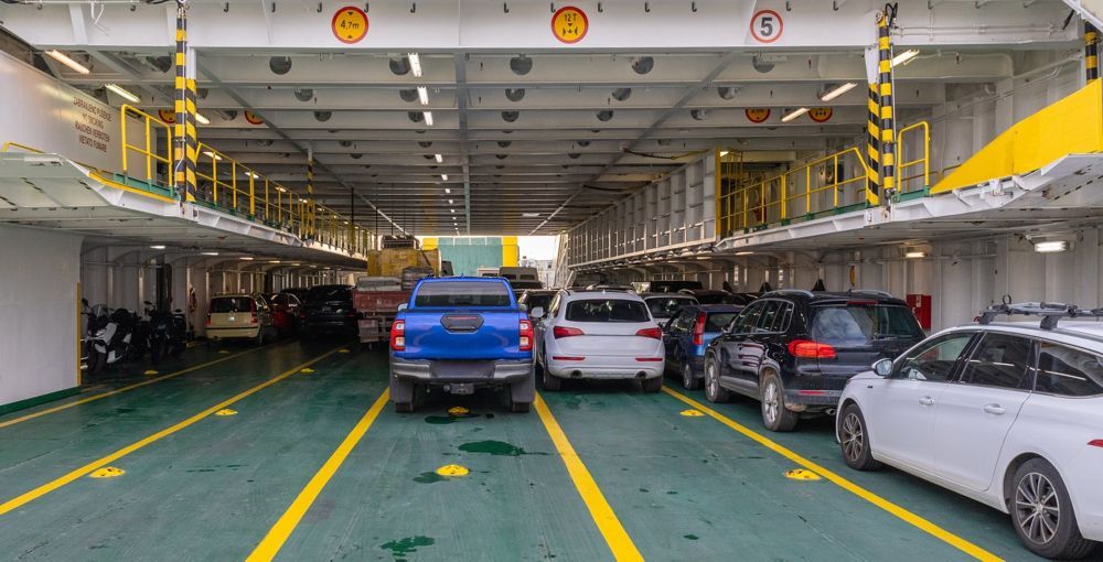 Cars lined up on the deck of a ferry. Yellow stripes and support beams are overhead.