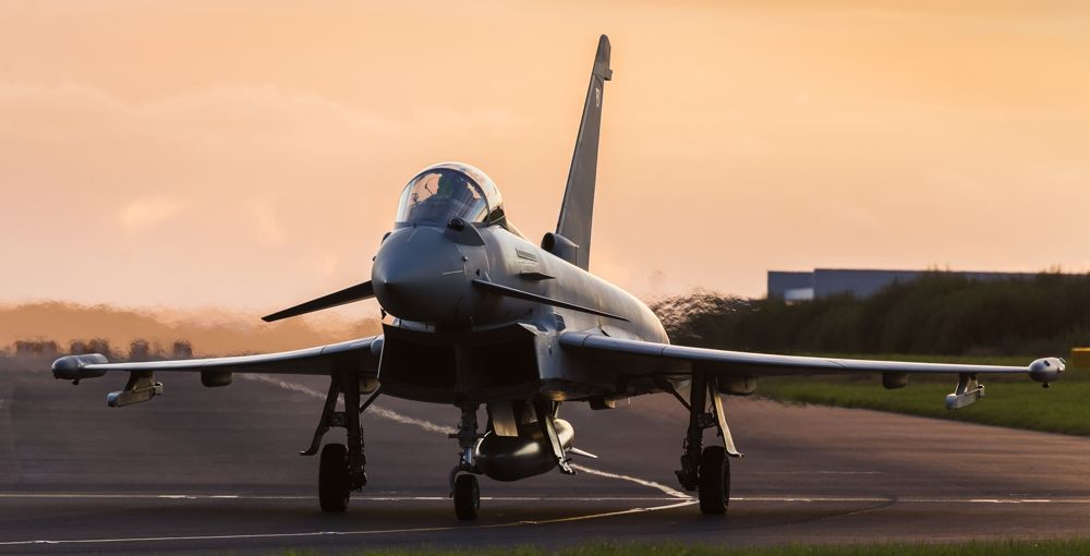 Eurofighter Typhoon jet on a runway, sun setting in background.
