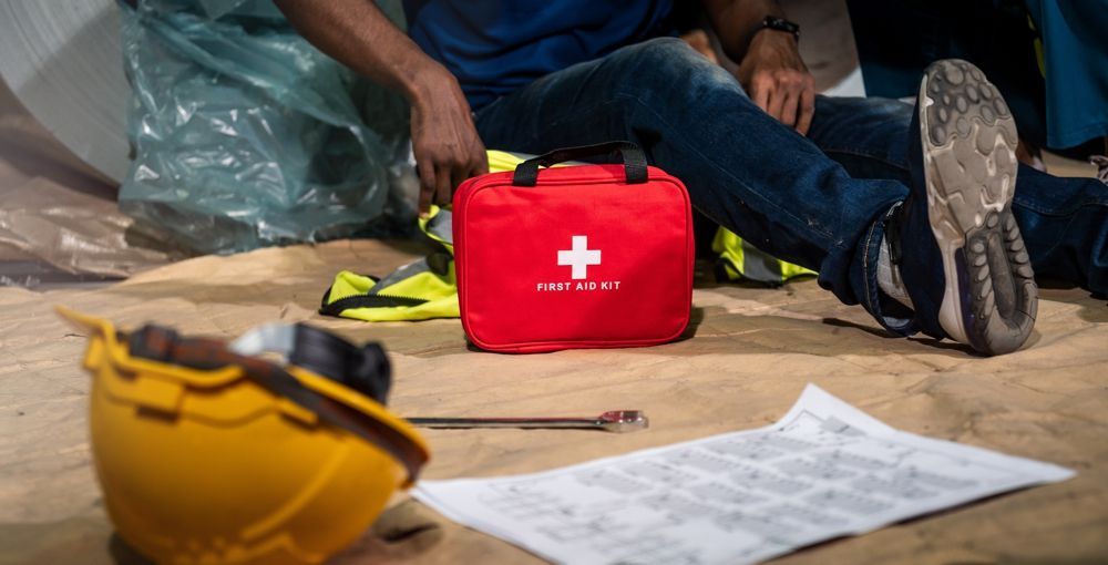 Person sits near a red first aid kit, work helmet, and blueprints.
