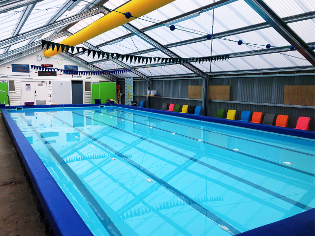 Indoor swimming pool with clear water, blue lane lines, and colorful seating along the side.