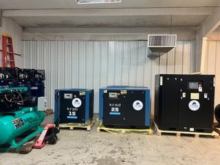 Three air compressors are sitting on pallets in a room.