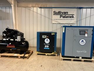 Three air compressors are sitting on wooden pallets in a warehouse.