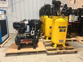 A bunch of air compressors are sitting on pallets in a room.