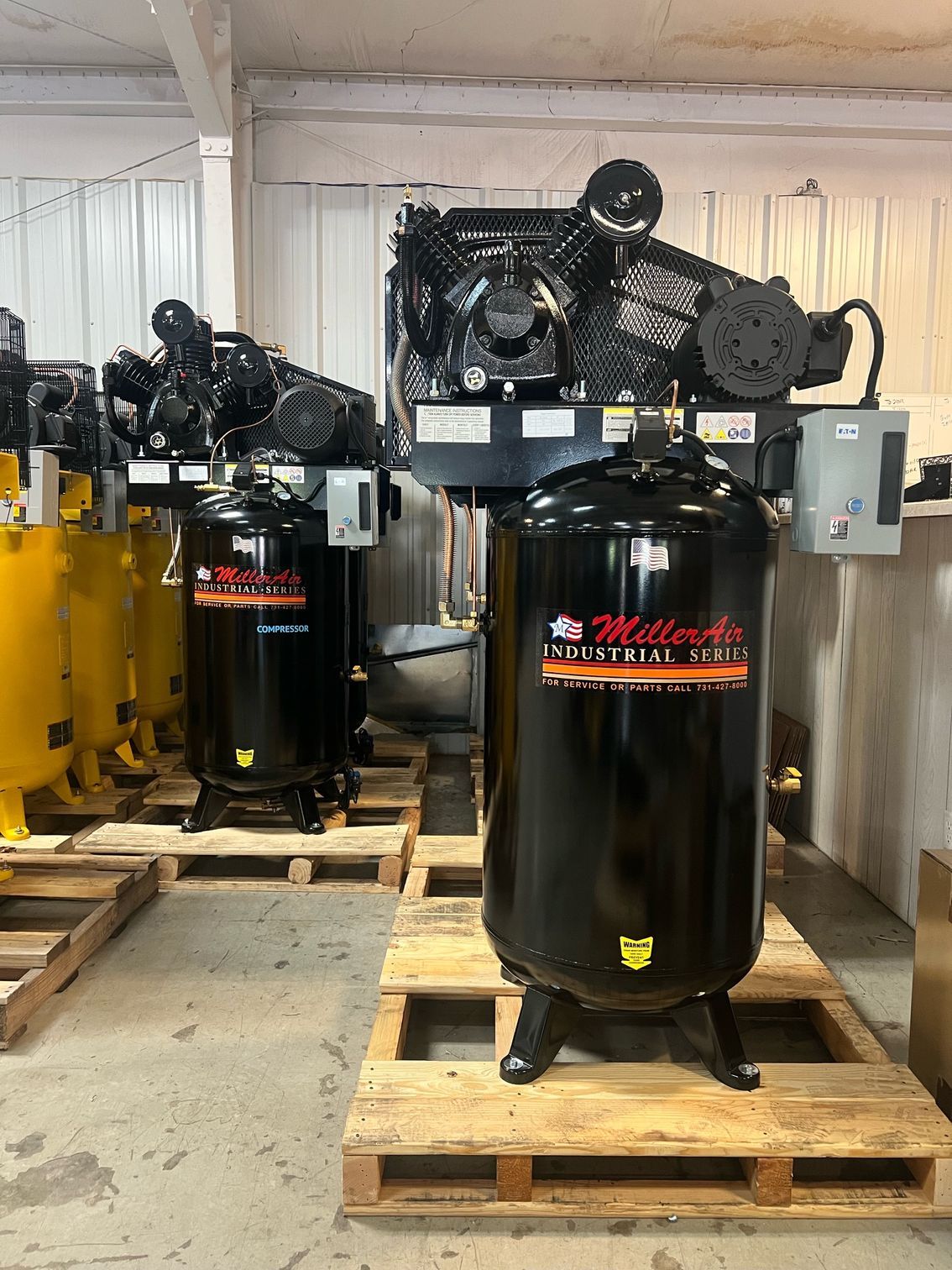 A bunch of air compressors are sitting on wooden pallets in a room.
