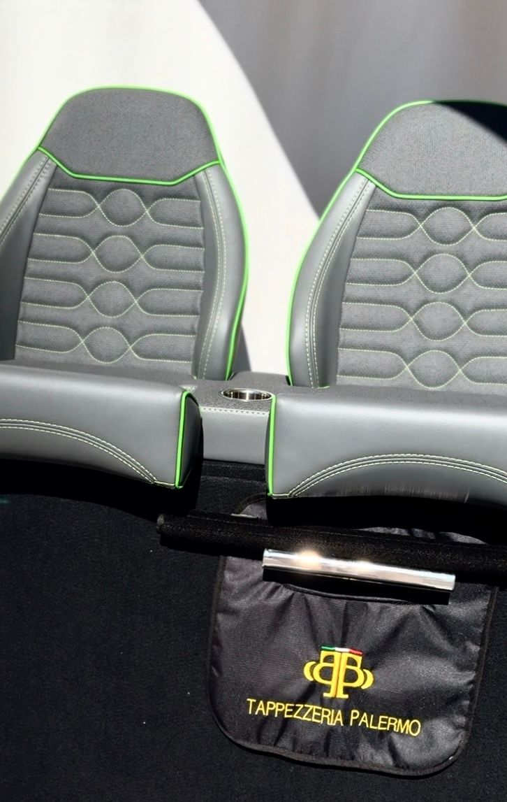 Sedili da barca grigio e neri con finiture verdi e una borsa nera con logo dorato.