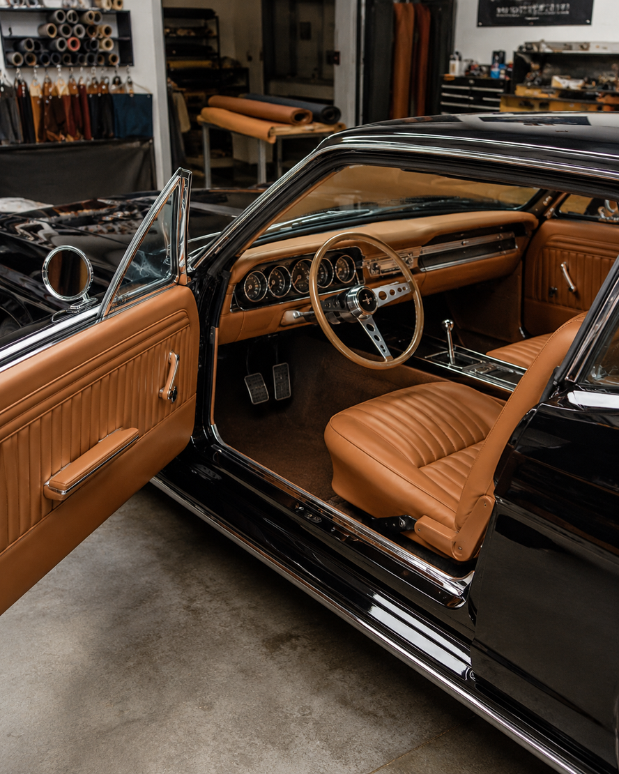 Auto d'epoca nera con la portiera aperta, che mostra gli interni in pelle color cuoio e il volante in un garage.