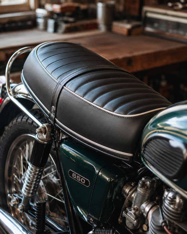 Primo piano di una sella da moto nera e dettagli cromati su una moto d'epoca in interni.