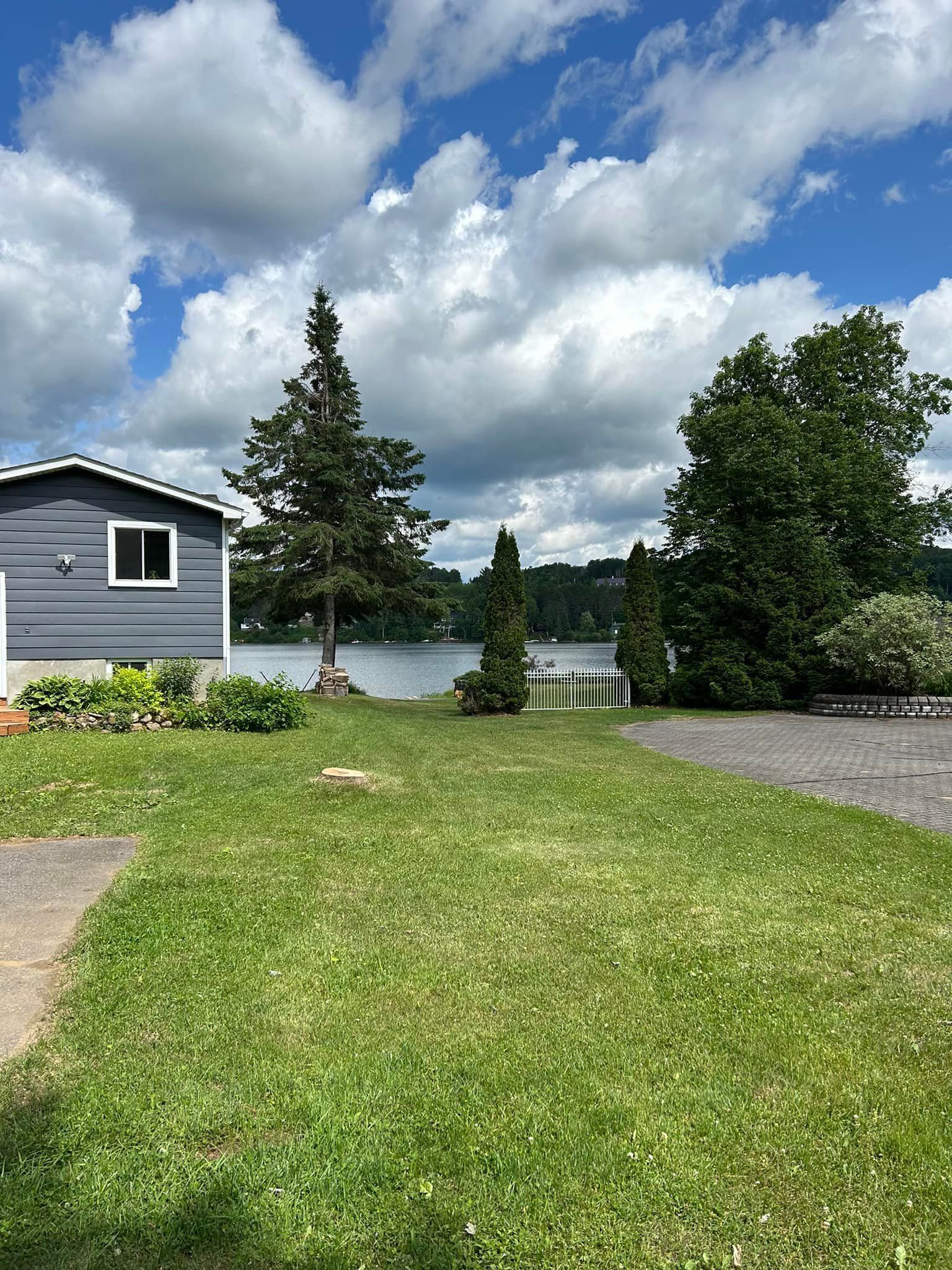 Blue house with a green lawn, trees, and a lake under a cloudy blue sky.