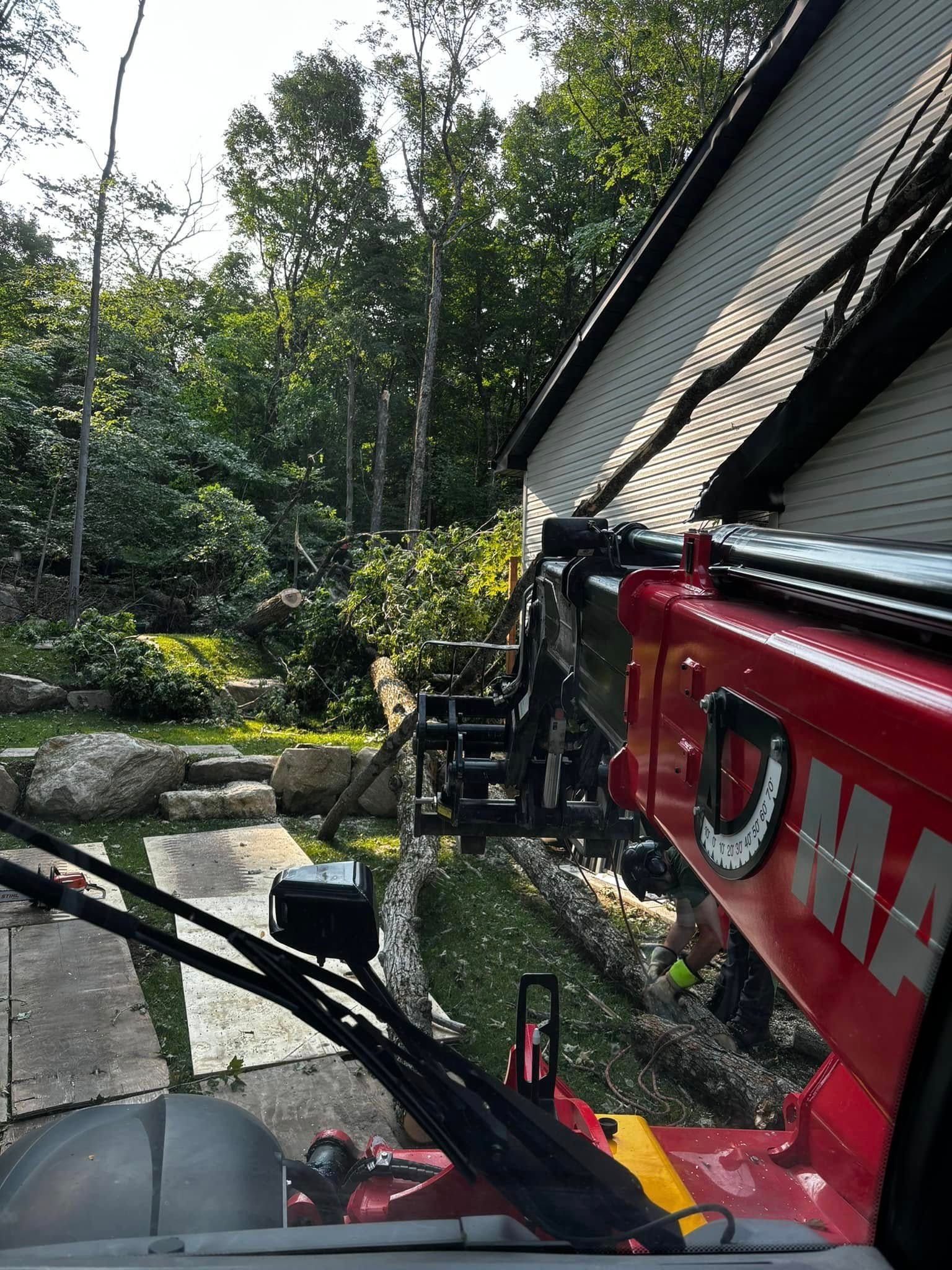 A red Manitou telescopic handler operating near a house, trees in the background.