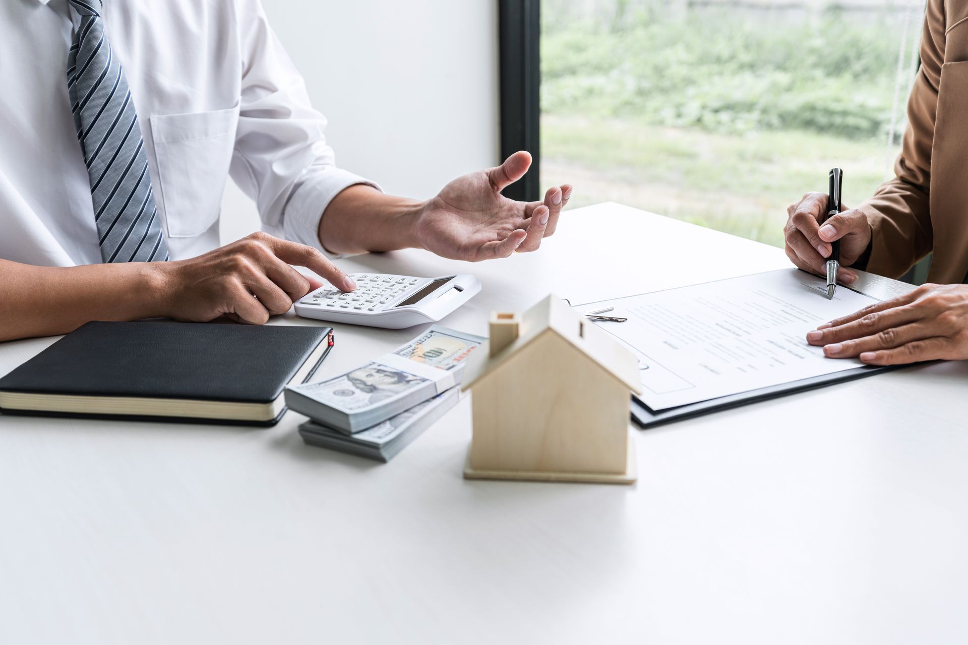 Man calculating with money and calculator. Woman signing document at table with house model.