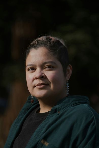 Person in a dark teal jacket, softly lit against a dark blurred background.