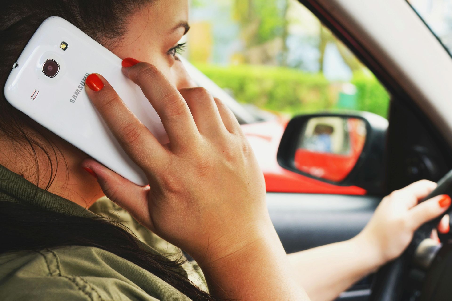 Woman driving a car while talking on a white smartphone, seen from the side in the driver’s seat