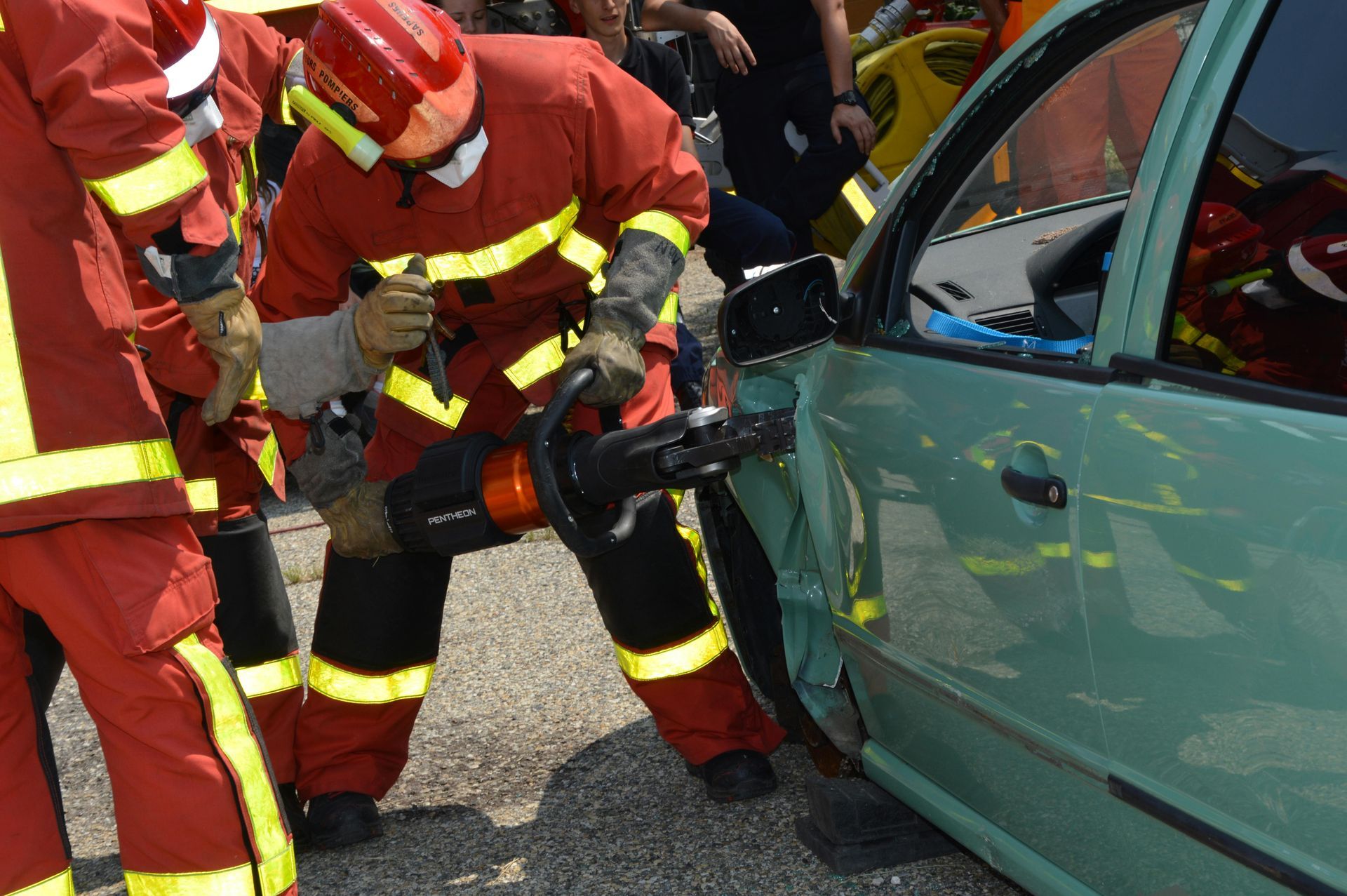 Firefighters using hydraulic cutters to rescue someone from a green car after a crash
