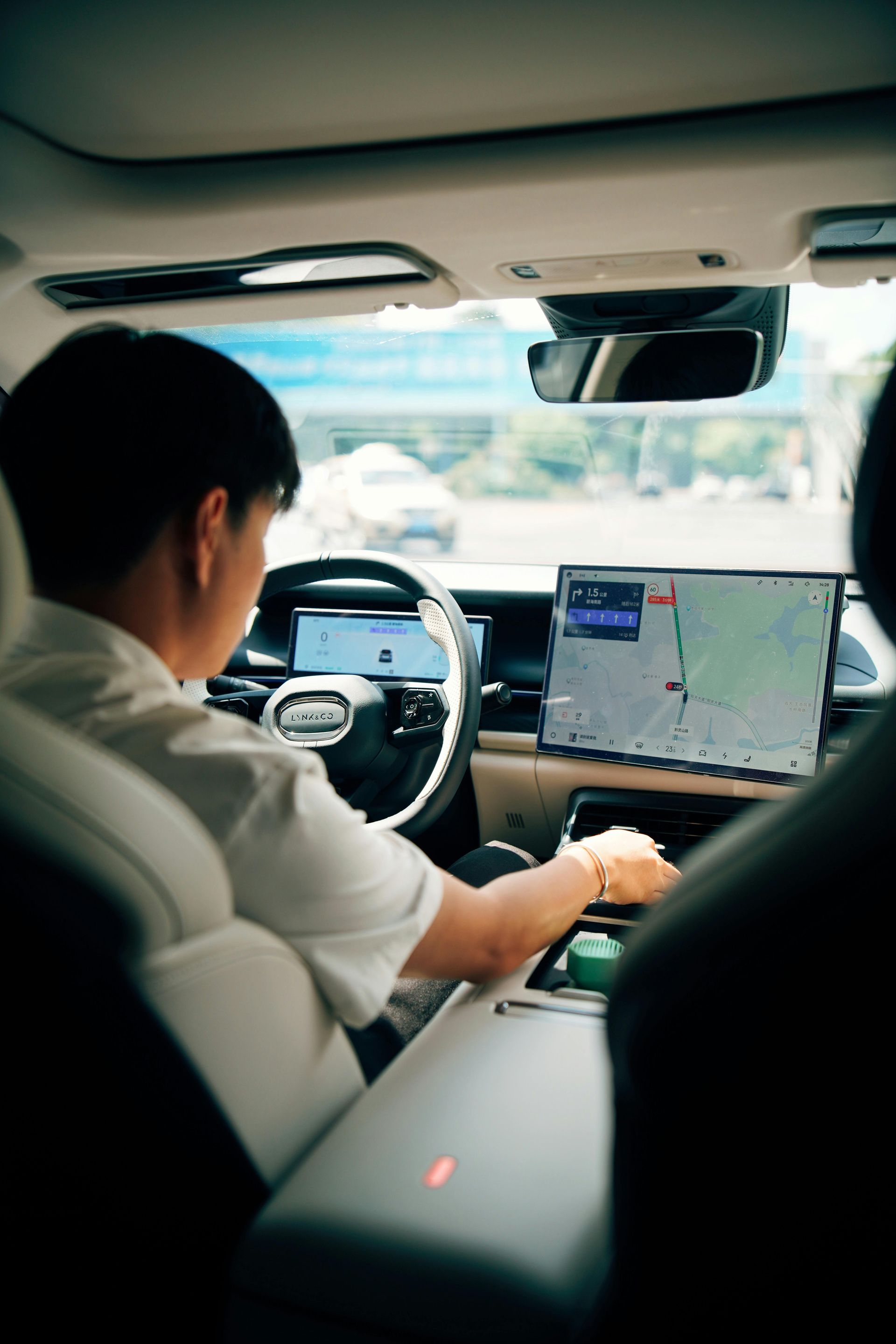 Driver using a laptop-style dashboard display in a car interior, with a steering wheel and road view ahead