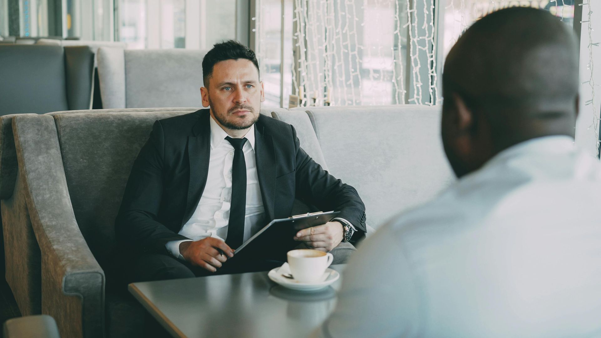 Two people in a meeting, one holding a tablet across a coffee table in a modern office lounge.