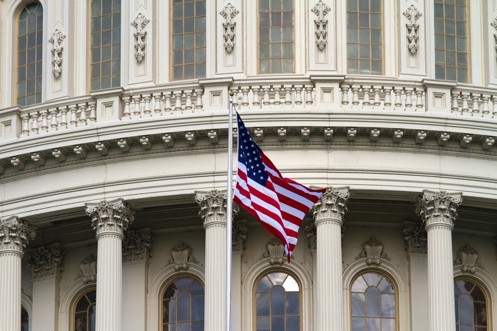 U.S. flag flying in front of an ornate white neoclassical building facade with columns and arched windows