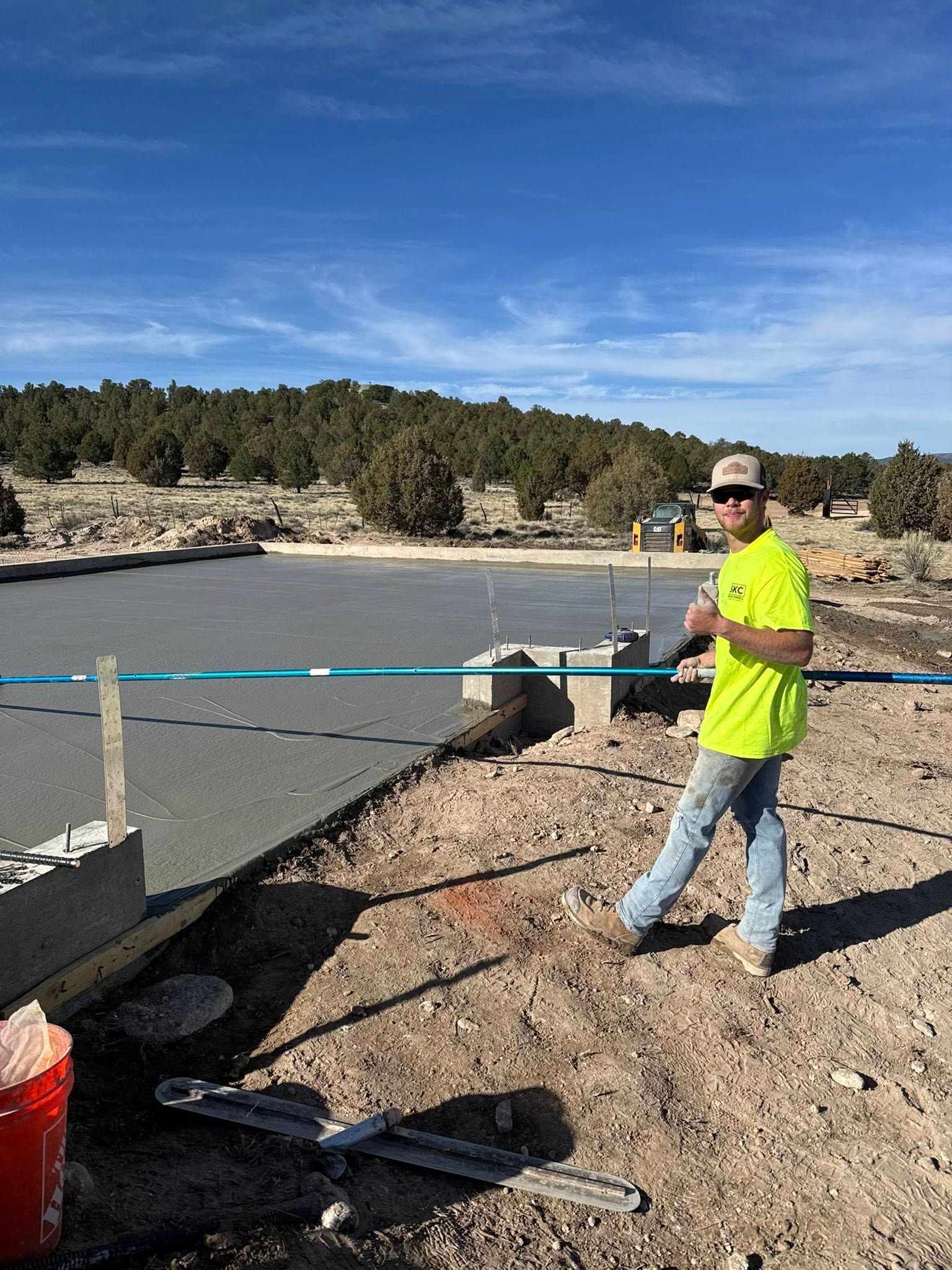 A construction worker is standing on top of a dirt field next to a body of water.