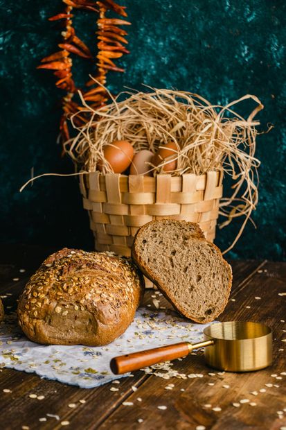 Panes rústicos y pan de molde en una cesta de mimbre con huevos y trigo sobre una mesa de madera.