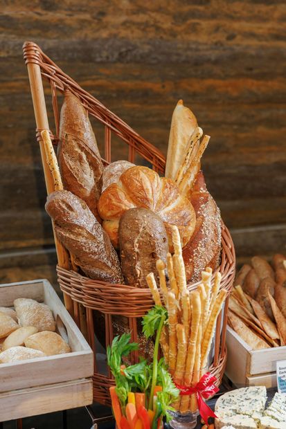 Cesta con baguettes y pasteles variados en el mostrador de una panadería, con palitos de pan recién hechos al frente.