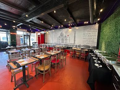 Restaurant interior with tables and chairs, buffet, and a Taj Mahal mural on the wall.
