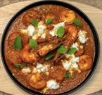 Shrimp in tomato sauce with feta cheese and mint leaves. Served in a black dish.