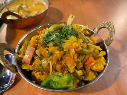 Close-up of Indian vegetable curry in a decorative metal bowl, featuring green peppers, onions, and cilantro.