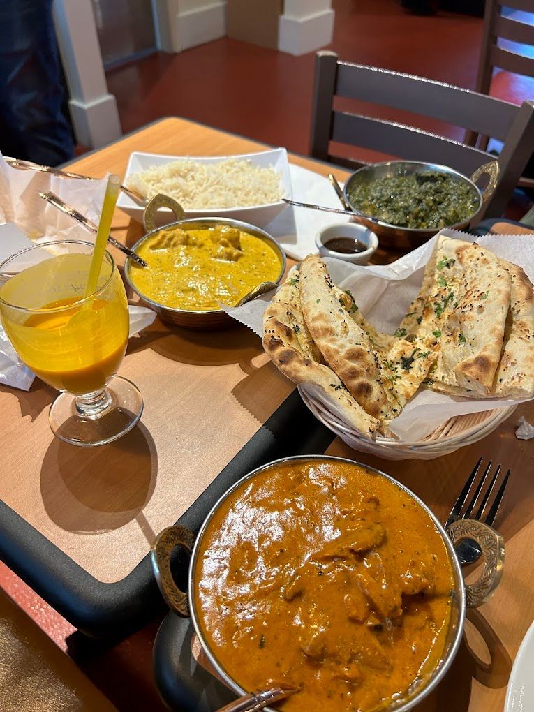 Table with Indian food: curries, rice, naan, spinach, drink. Wooden table in a restaurant setting.