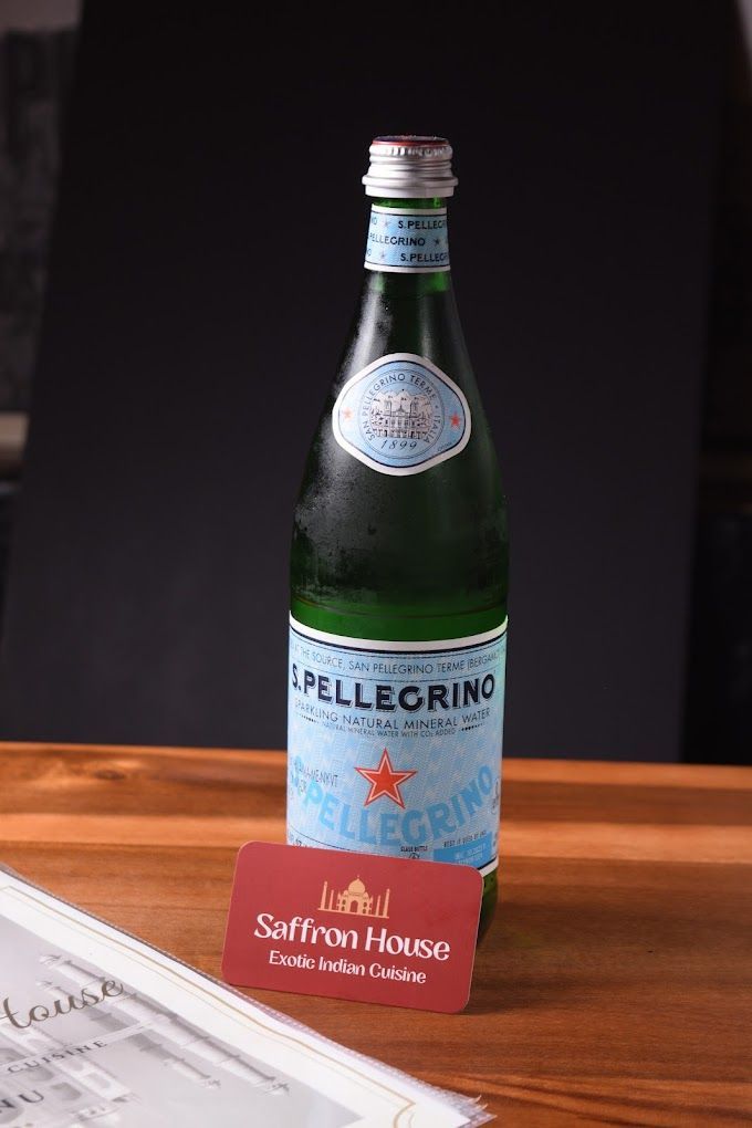 Bottle of S. Pellegrino water on a wooden table with a Saffron House card and menu.