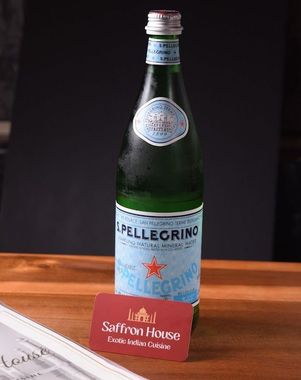 Bottle of San Pellegrino mineral water and a business card for Saffron House restaurant on a wooden surface.