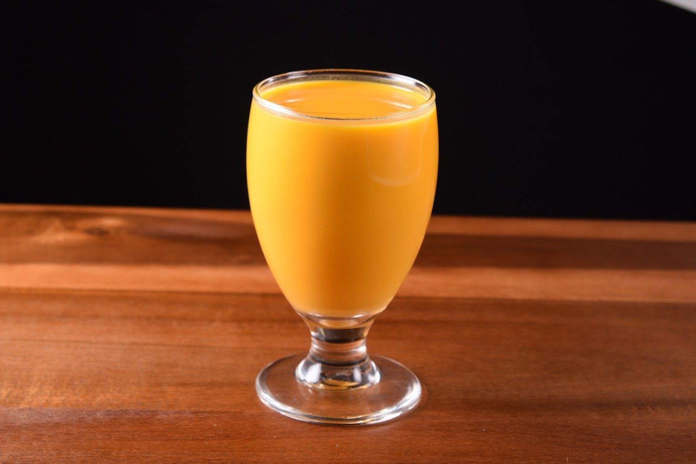 Glass of orange liquid on wooden table, black background.