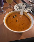 Bowl of orange soup with spoon on a table set for a meal.