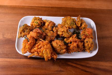 Golden-brown pakoras on a white plate, set on a wooden surface.