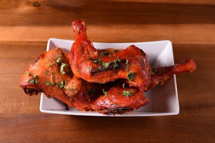 Roasted chicken legs on a white plate, sprinkled with herbs, on a wooden surface.