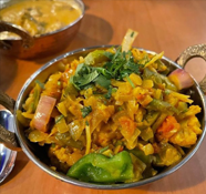 Close-up of a mixed vegetable curry in a metal bowl, with visible peppers, cauliflower, and herbs.