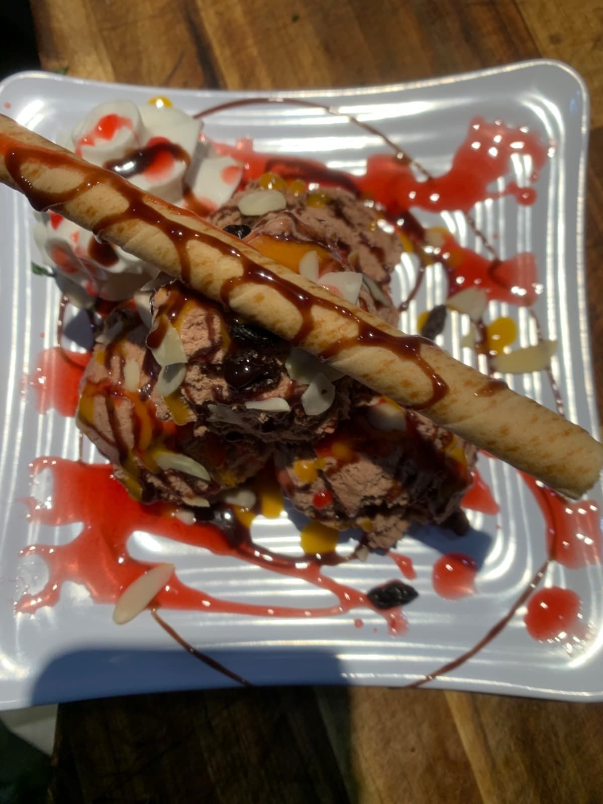 Ice cream sundae on a square white plate, drizzled with chocolate and strawberry sauce, topped with a wafer.