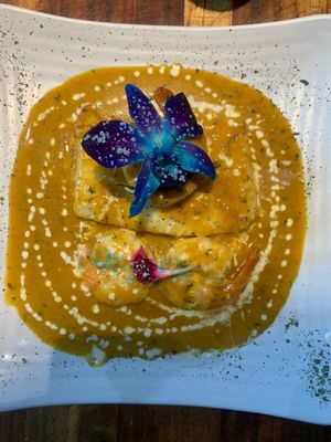 Dish with orange sauce, layered components, and blue flower garnish on white plate.