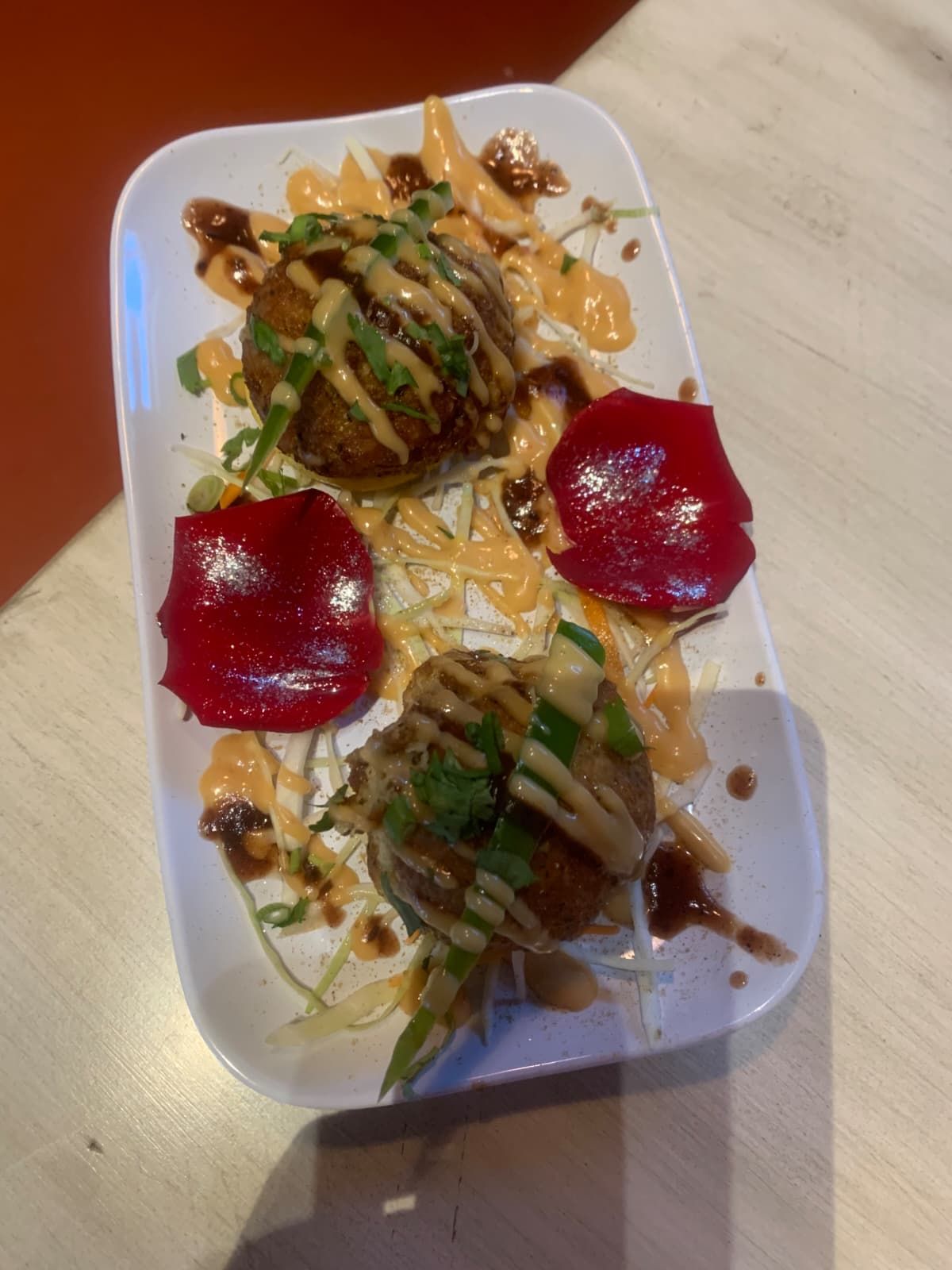 Appetizer: Three round, fried food items on a white plate, drizzled with sauce and garnished with red peppers.