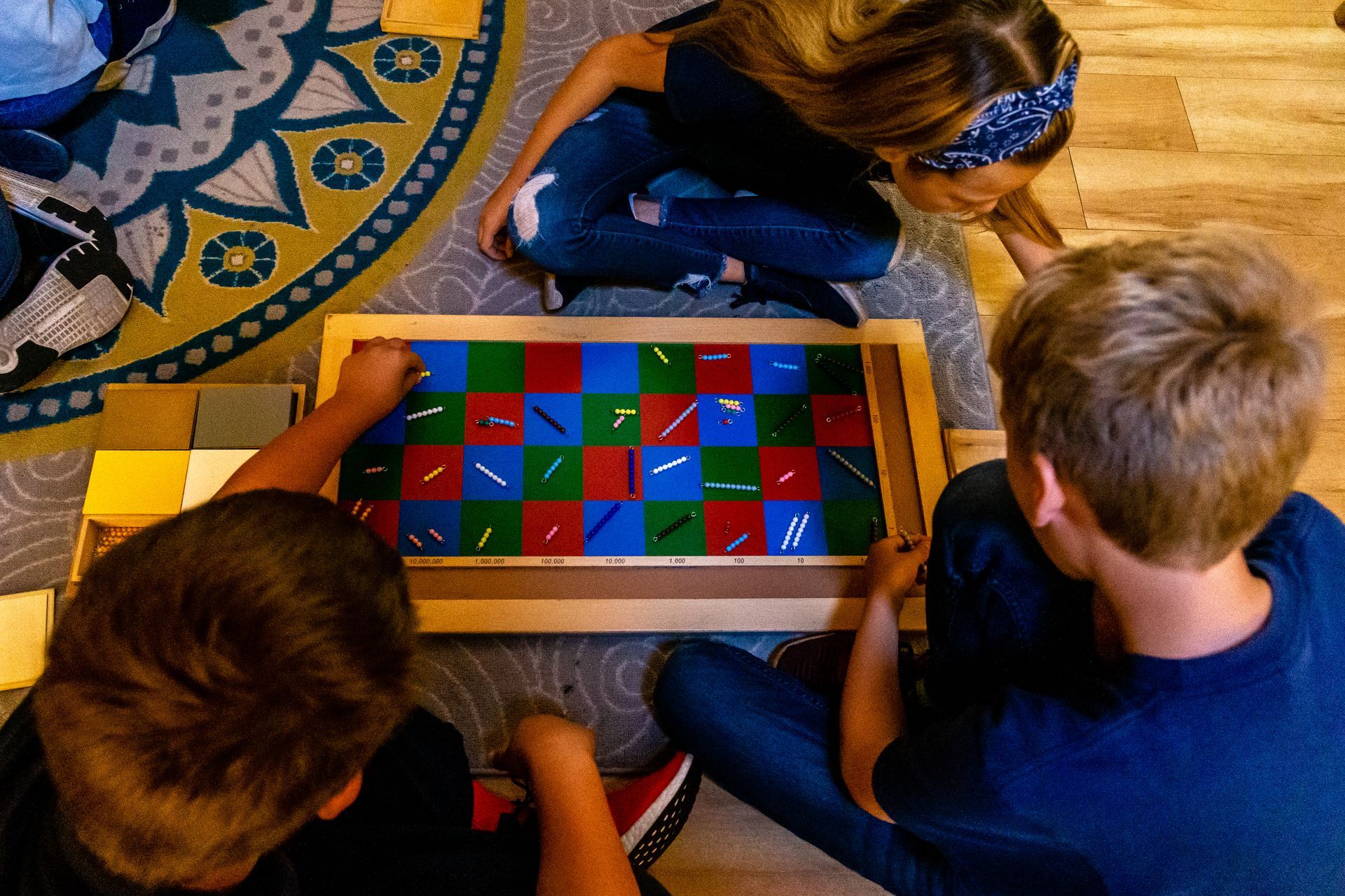 A group of Montessori children are sitting on the floor working on math beads.