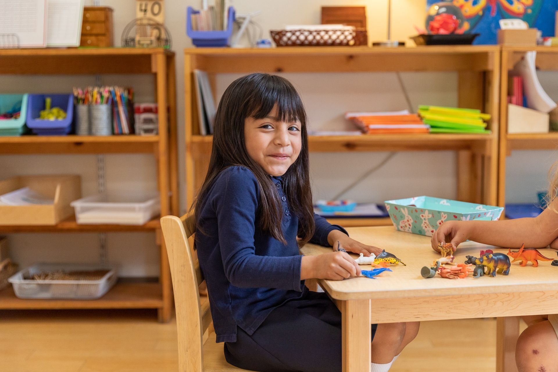 Montessori child is sitting at a table in a classroom playing with toys