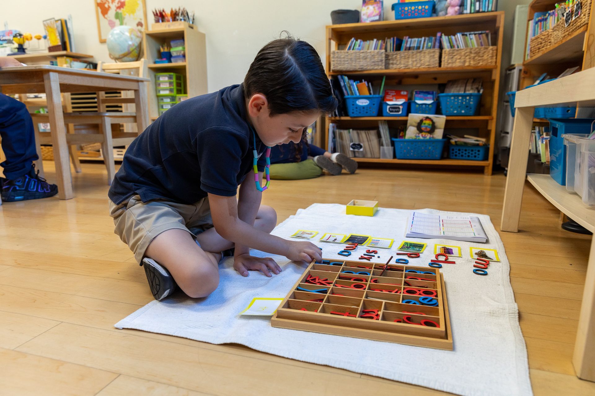 Montessori child is sitting on the floor in a classroom playing with toys