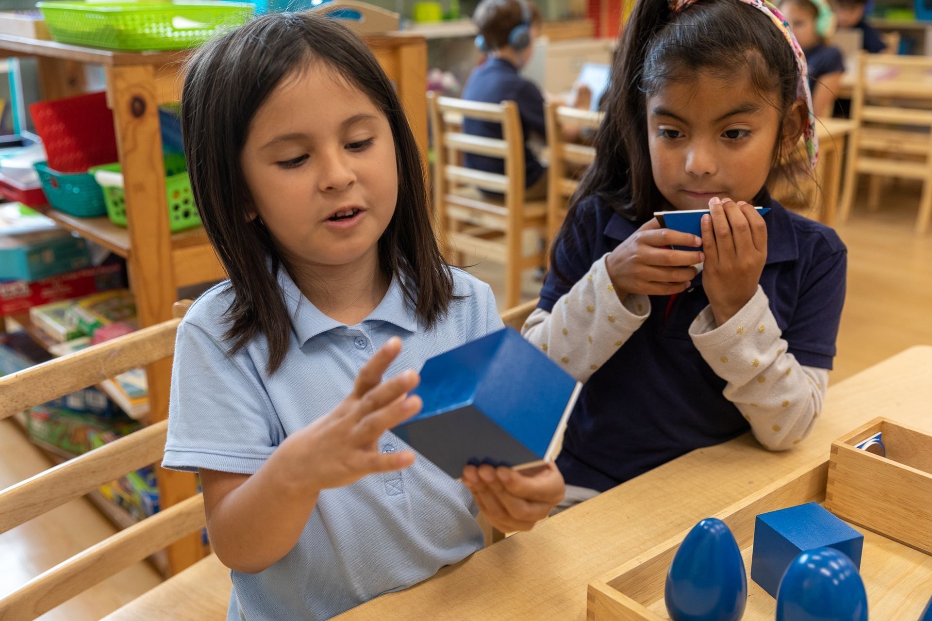 Two Montessori children are working with geometric blocks in a classroom.