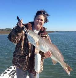 Smiling angler holding a large silver fish on a boat in bright daylight