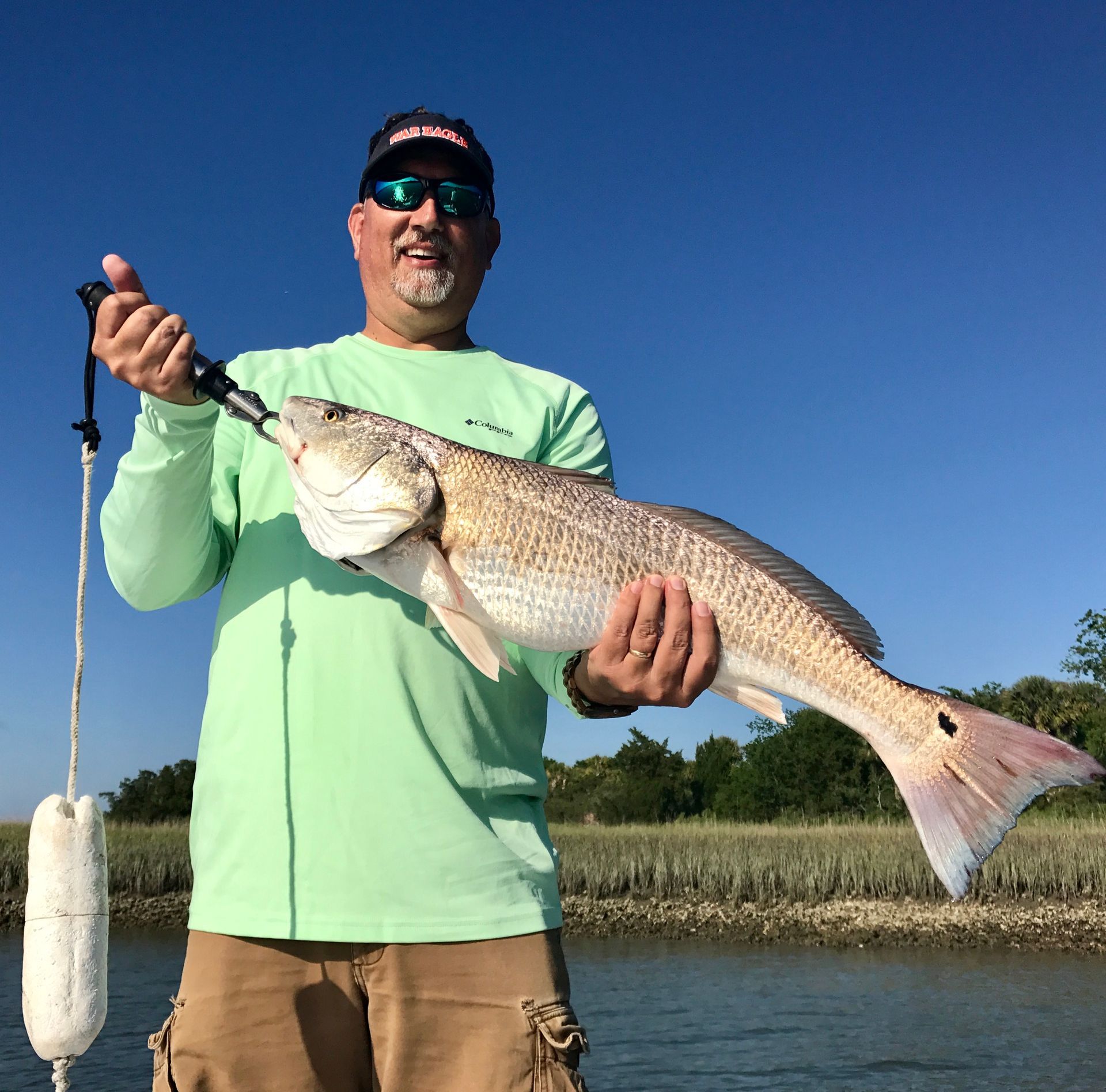 Angler holding a large silver fish on a boat under a clear blue sky