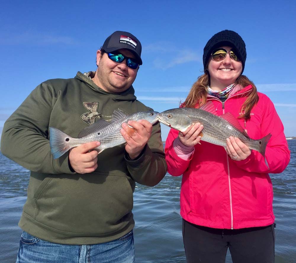 Two people on a boat holding fish, smiling in cold blue water under a clear sky